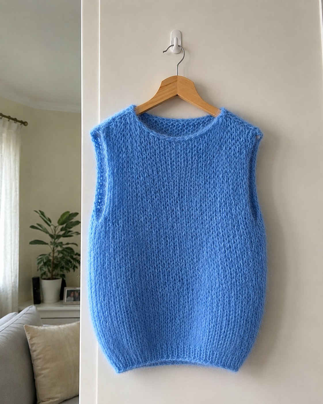 Sky blue brushed mohair knitted vest with ribbed hem and wide round neck, hanging on a wooden hanger