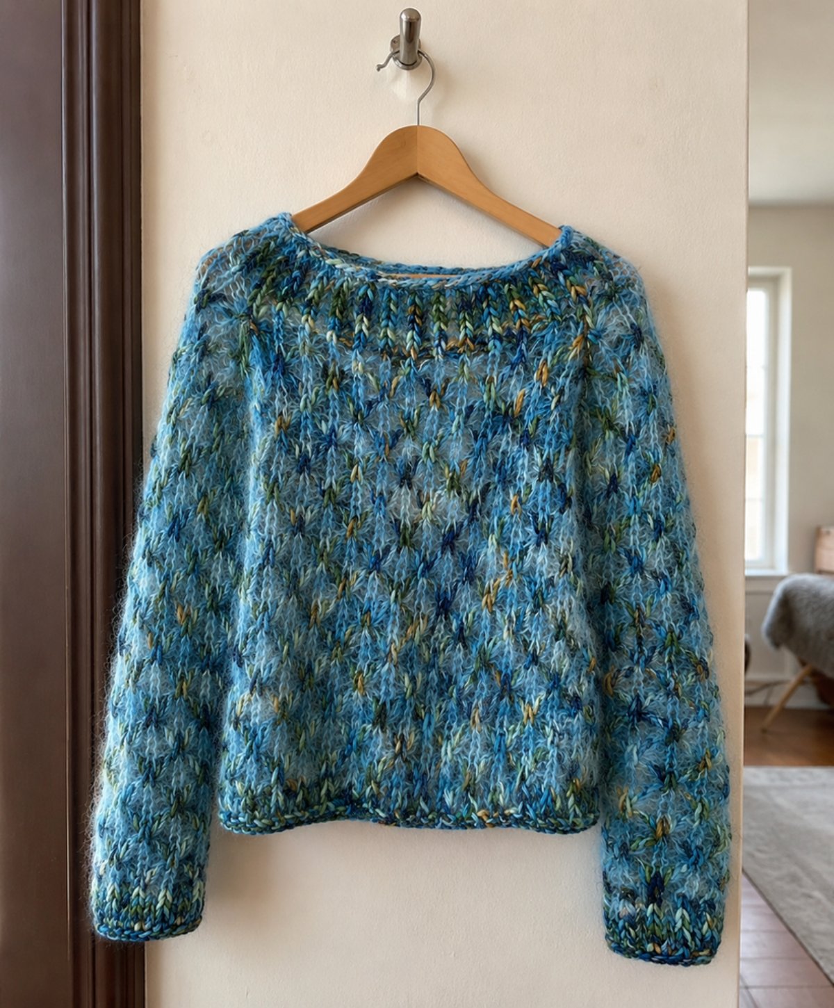 Sea blue cluster-stitch knitted sweater in variegated art yarn with mohair haze, hanging on a wooden hanger